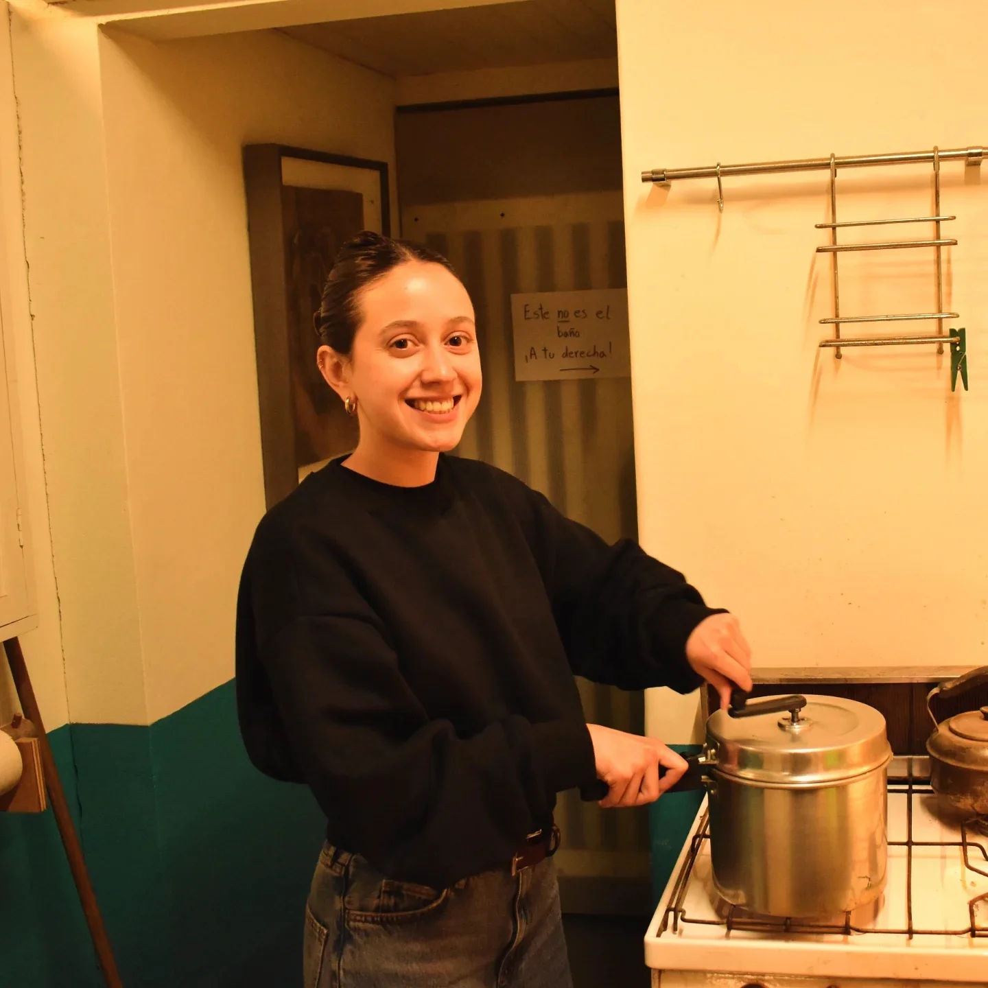Alguien sonríe junto a la cocina del taller con la olla del pochoclo destapada, al lado de un cartel escrito a mano que aclara «Este no es el baño, ¡a tu derecha!»