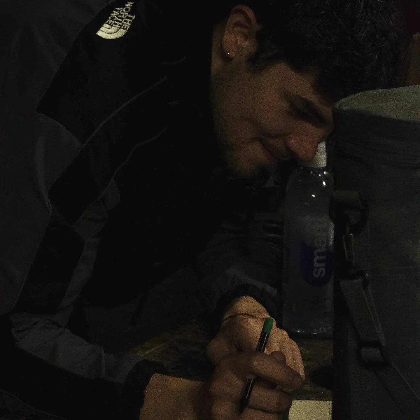 Alguien inclinado sobre el papel, escribiendo su respuesta con una birome en la penumbra