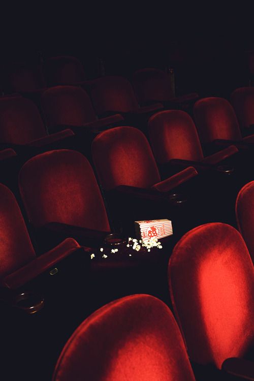 Una sala de cine vacía: butacas rojas a oscuras y una caja de pochoclo volcada sobre un asiento